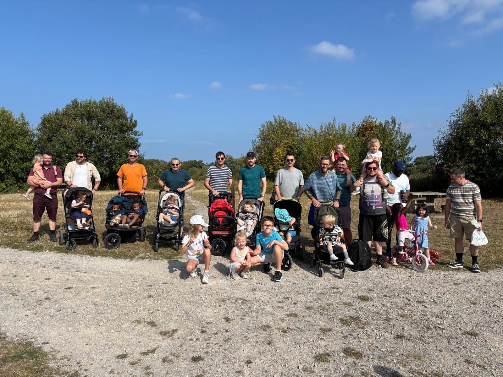 Families with children and pushchairs gathered outdoors on a sunny day